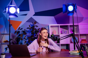 Young professional woman at work as a media influencer recording a podcast in a vibrant home studio...