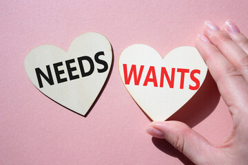 Wants and Needs symbol. Concept word Wants and Needs on wooden hearts. Businessman hand. Beautiful pink background. Business and Wants and Needs concept. Copy space