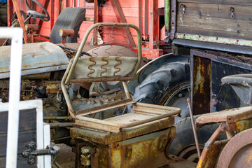 Rusty seat of an old tractor with exposed springs and no upholstery. Background shows parts of...