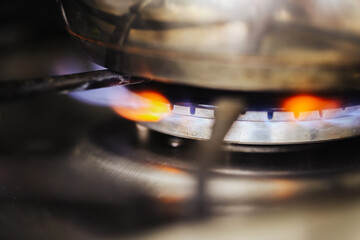 Close-up of gas burner. Blue and orange flames heating metal pot. Kitchen stove in use. Cooking...