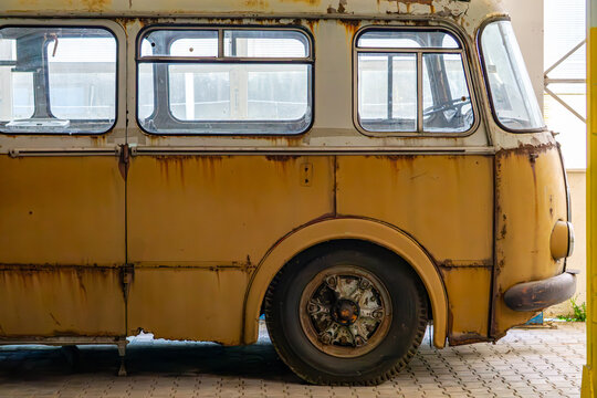 Rusty side of an old yellow bus in an abandoned building, with visible windows and wheel details.