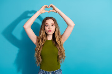 Young woman making a heart gesture with hands while posing against a vibrant blue background in...