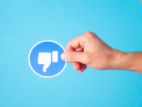 Online disapproval: human hand holding a "dislike" sign on a blue surface.