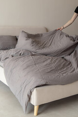 A woman makes the bed. Soft focus. Grey boiled cotton bed linen