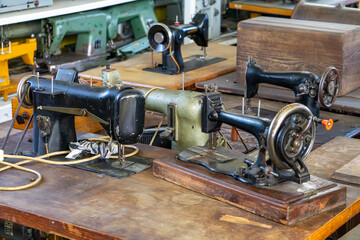 Old sewing machines on wooden tables. Vintage tailoring equipment with hand and foot drive.