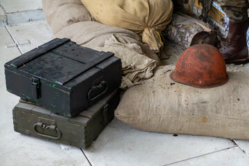 Old military transport crates, canvas sacks, and a rusty helmet on a white floor – vintage...