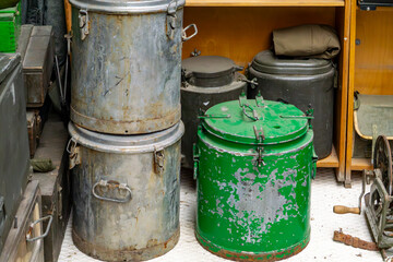 Old military food containers and metal thermoses, including a green field kitchen pot – vintage cooking equipment from the communist era stored indoors.
