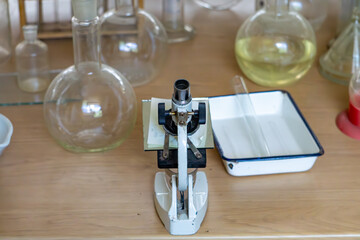 Vintage microscope on a laboratory table, surrounded by glass flasks and an enamel tray. Retro...