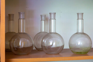 Vintage glass laboratory flasks with round bottoms and narrow necks placed on a wooden shelf. Old...