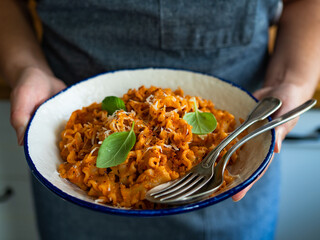 Woman holding plate with creamy tomato and stracciatella reginelle noodles, close-up