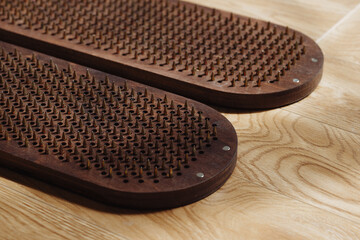 Two brown wooden acupressure boards with metal spikes placed on a light wooden floor. Close-up with...