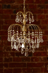 Gold chandelier with crystal drops hanging in a rustic setting. Brick wall background, warm tones,...
