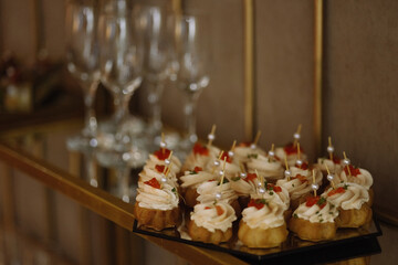 Small canapes with cream and red caviar on a mirrored tray near empty champagne glasses. Warm...