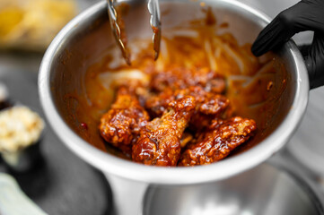 Close-up of crispy chicken wings coated in glossy sauce, tossed in a stainless steel bowl with...