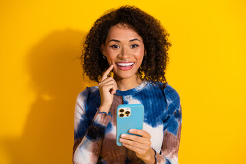 Smiling Woman Holding Smartphone Against Yellow Background Exuding Confidence and Charm in Colorful...
