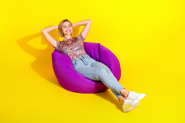 Young woman relaxing on a purple bean bag chair against a vibrant yellow background, embodying...