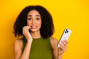 Young woman with curly hair holding a smartphone and expressing nervousness against a vibrant...
