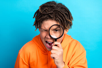 Curious young schoolboy holding a magnifying glass in front of his eye with a playful expression...