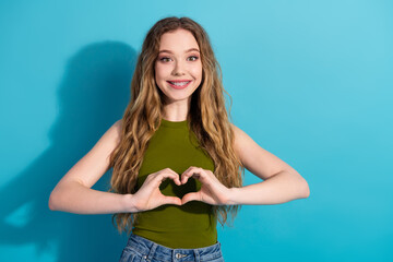 Happy young girl in casual attire making a heart gesture with her hands on a blue background