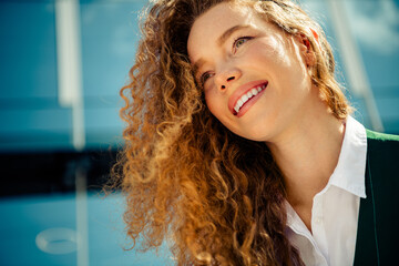 Cheerful businesswoman with curly hair smiling warmly outdoors with urban background