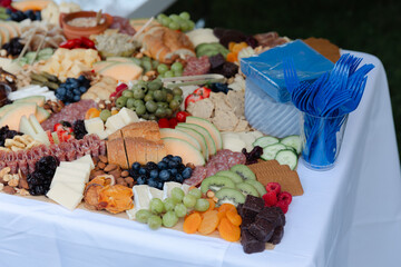 Colorful display of assorted cheese, meats, fruits, and crackers at an outdoor catering event