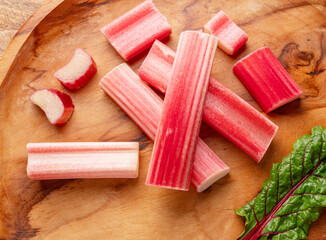 Cuts of red rhubarb stem on wooden plate on the table, top view.