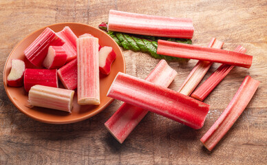 Cuts of red rhubarb stem on wooden plate on the table, top view.