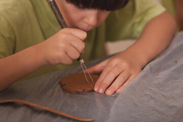 Boy using sculpting tool to carve clay during creative activity