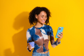 Attractive young woman enjoying her leisure time while using a smartphone and holding a coffee cup...