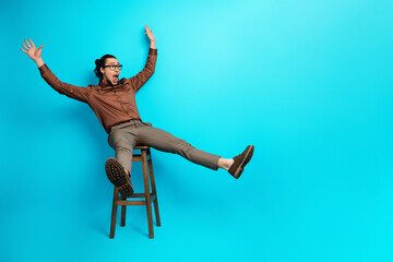 Young businessman on stool with surprised expression against vibrant turquoise background in smart...