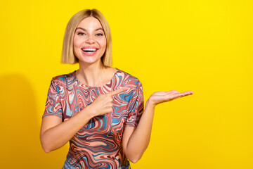 Smiling young woman with blonde bob hairstyle gesturing on yellow background in a vibrant patterned...