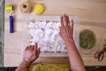 Woman placing torn white paper into water container for pulp making. DIY handmade paper preparation...