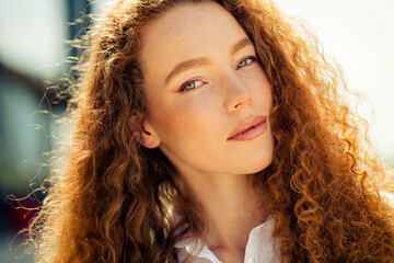 Young elegant woman with curly red hair photographed outdoors on a sunny day, exuding confidence...