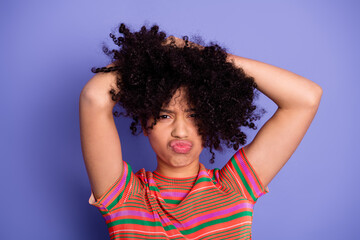 Young woman with expressive curly hair wearing colorful striped t-shirt poses playfully against...