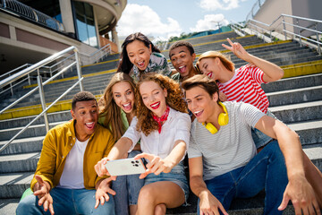 Joyful friends taking a selfie while sitting on stairs outdoors in an urban environment on a sunny...