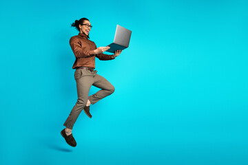 Young professional man joyfully showcasing a laptop against a vibrant turquoise background...