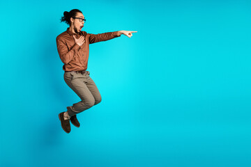 Young male entrepreneur in brown shirt expressing surprise on turquoise background, pointing with excitement and enthusiasm