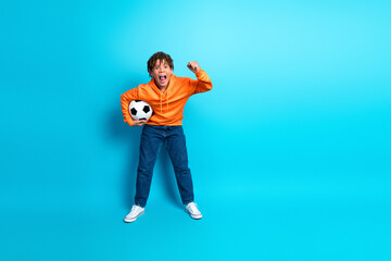 Energetic young boy holding a soccer ball against a vibrant blue background wearing a stylish...