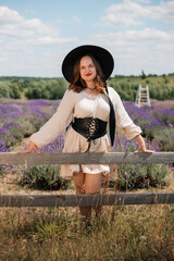 Woman in a white dress and black hat poses in a lavender field on a sunny day during summer