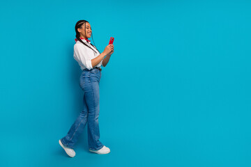 Young stylish woman with braided hair using a red phone against a vibrant blue background in casual...