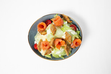Salad with salmon, iceberg lettuce, cherry tomatoes, wheat croutons, and creamy dressing on a plate, isolated on white background