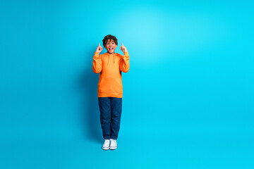 Happy schoolboy wearing orange hoodie shows gestures on blue background