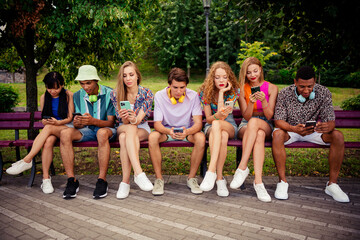A diverse group of young friends sitting together on a park bench enjoying a sunny day and bonding...
