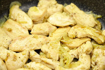 Sizzling pieces of seasoned chicken breast cooking in a frying pan with sauteed onions, showcasing a delicious meal preparation process in a modern kitchen setting