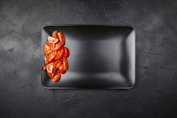 Freshly sliced tomatoes arranged on a sleek black plate, showcasing vibrant colors and textures,...