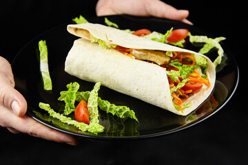 Delicious wrap filled with fresh vegetables and grilled chicken, served on a black plate, garnished with lettuce and cherry tomatoes, showcasing vibrant colors and appetizing presentation