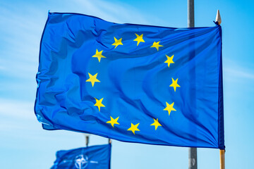 European Union flag waiving on a flagpole with NATO flag behind 