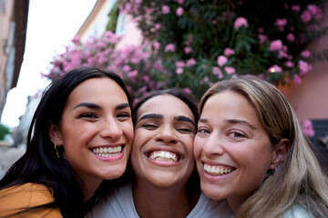Three cheerful young women posing together outdoors, their faces close and radiating joy, embodying...