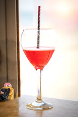 Refreshing red cocktail with striped straw on rustic wooden table in soft light