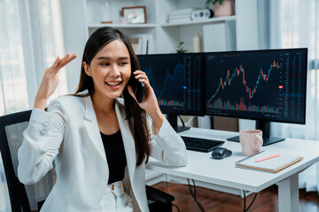 Young beautiful Asian businesswoman calling to broker on phone to analyze stable or higher profit...
